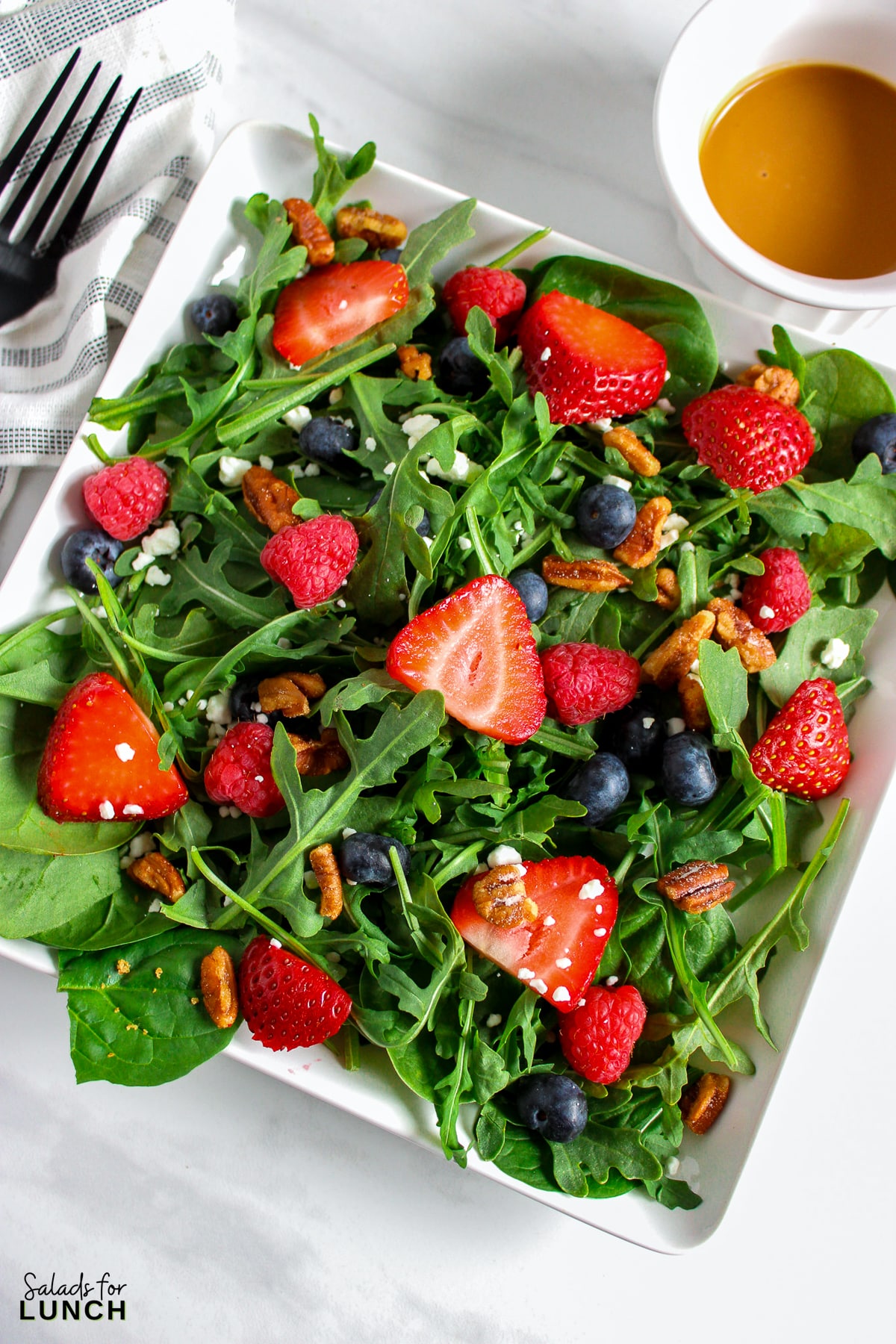 A salad with arugula,berries and honey roasted pecans topped with a creamy balsamic vinaigrette on a plate.