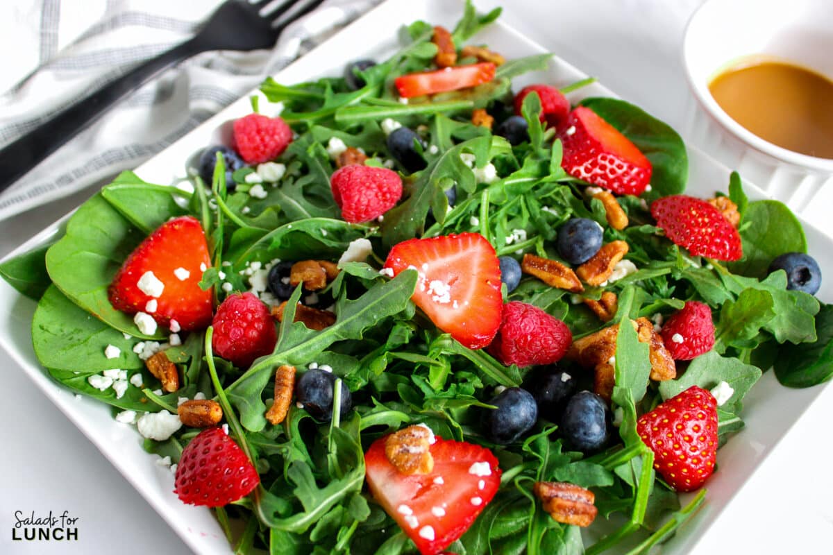 A salad with arugula,berries and honey roasted pecans topped with a creamy balsamic vinaigrette on a plate.